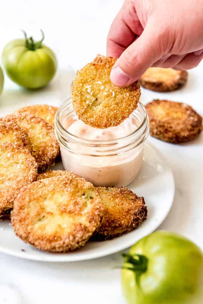 A hand dipping a sliced fried green tomato into a jar of dipping sauce