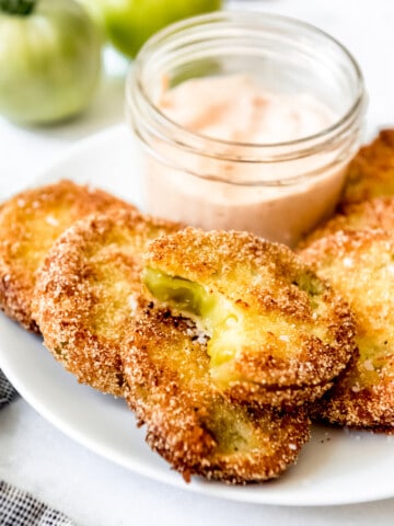 A small jar of dipping sauce on a white plate with sliced fried green tomatoes