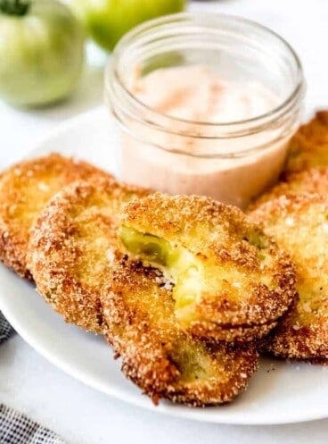 A small jar of dipping sauce on a white plate with sliced fried green tomatoes