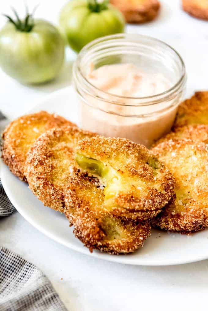 Fried green tomatoes on a white plate with a small jar of dipping sauce
