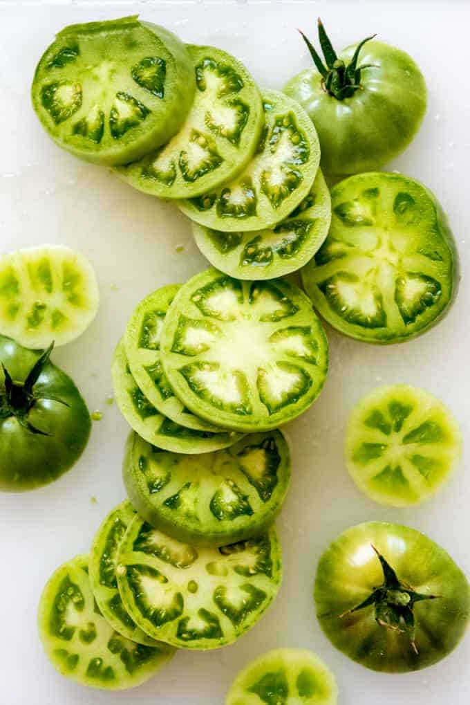 Sliced green tomatoes with some whole tomatoes to the sides