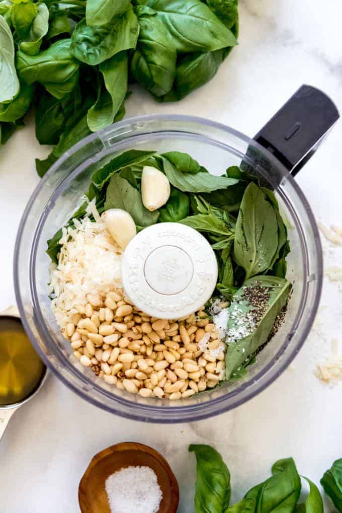 Basil leaves, garlic cloves, pine nuts, and grated parmesan cheese in the bowl of a food processor.