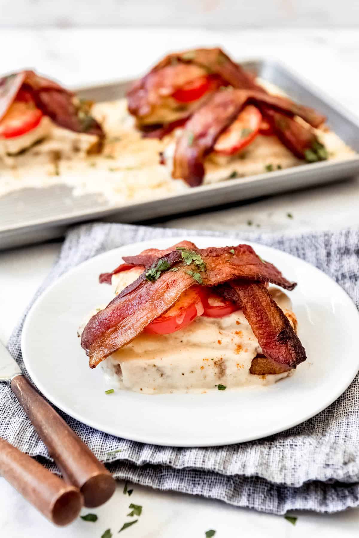 Kentucky hot brown sandwich on white plate, with pan of sandwiches in background.