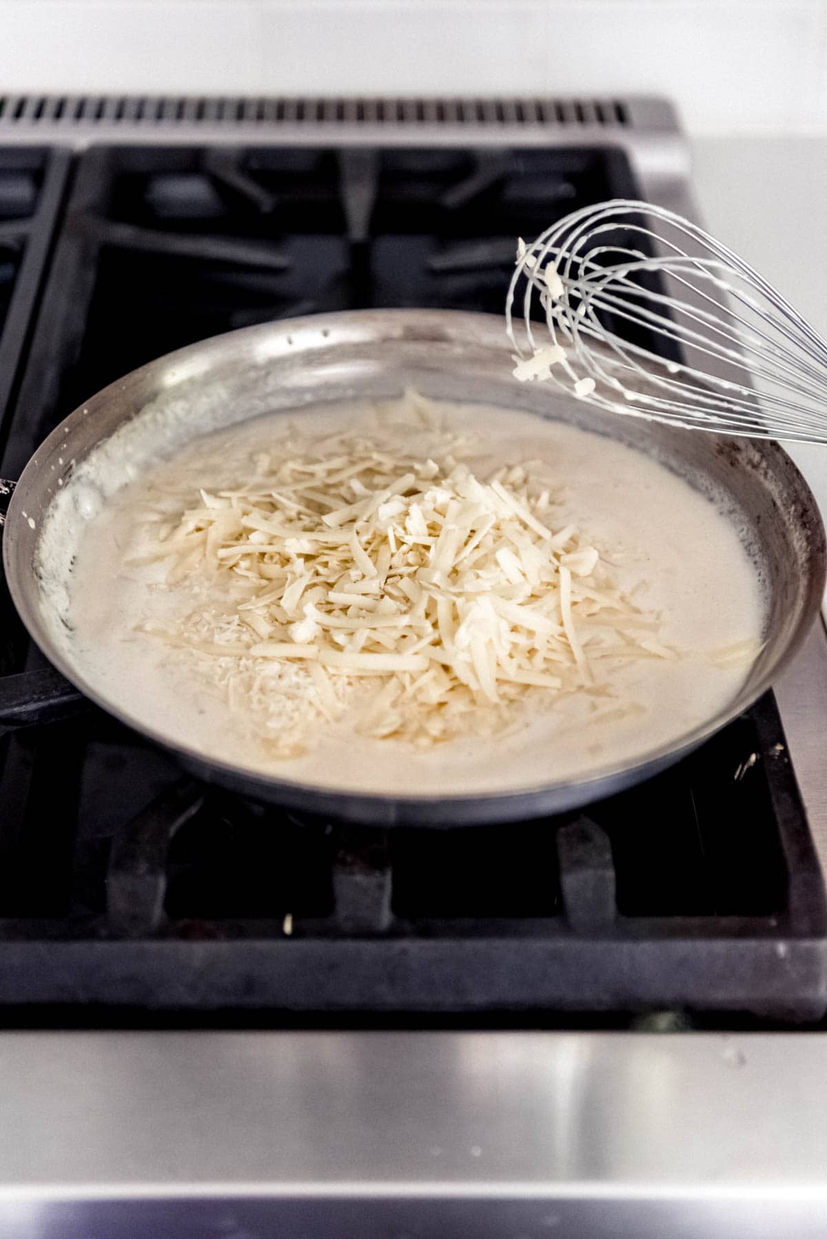adding cheese with a whisk to a skillet of mornay sauce on the stove.