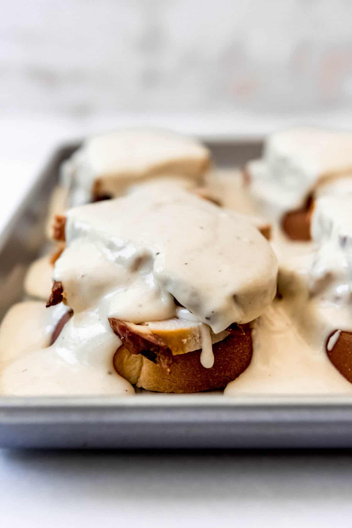 Mornay smothered over open faced sandwiches on a baking sheet.