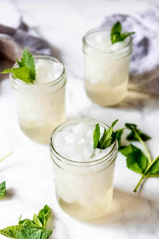 Pint-size mason jars filled with ice and non-alcoholic mint juleps next to mint leaves.