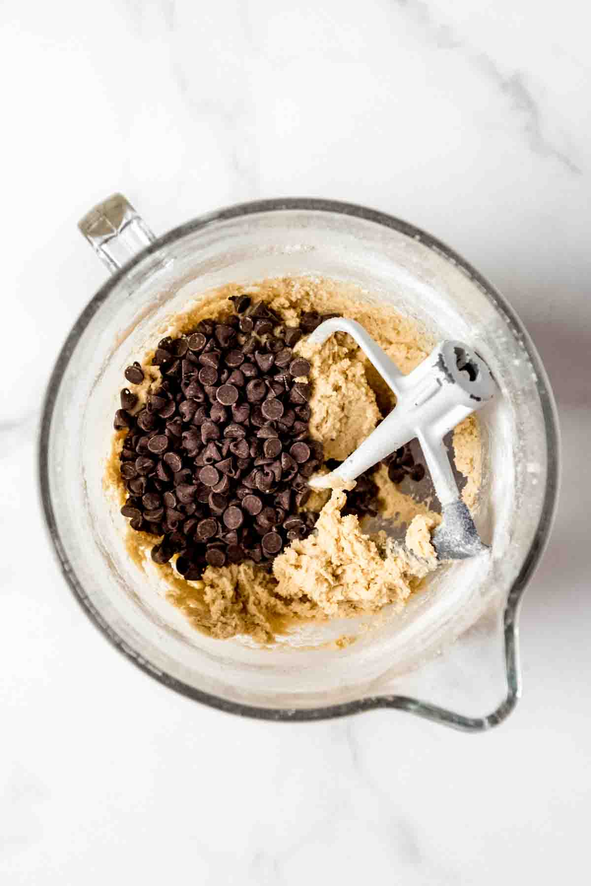 a bowl of cookie dough with chocolate chips and a paddle attachment resting inside