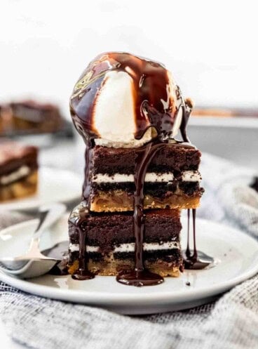 Two slutty brownies stacked on a plate with a scoop of vanilla ice cream on top.