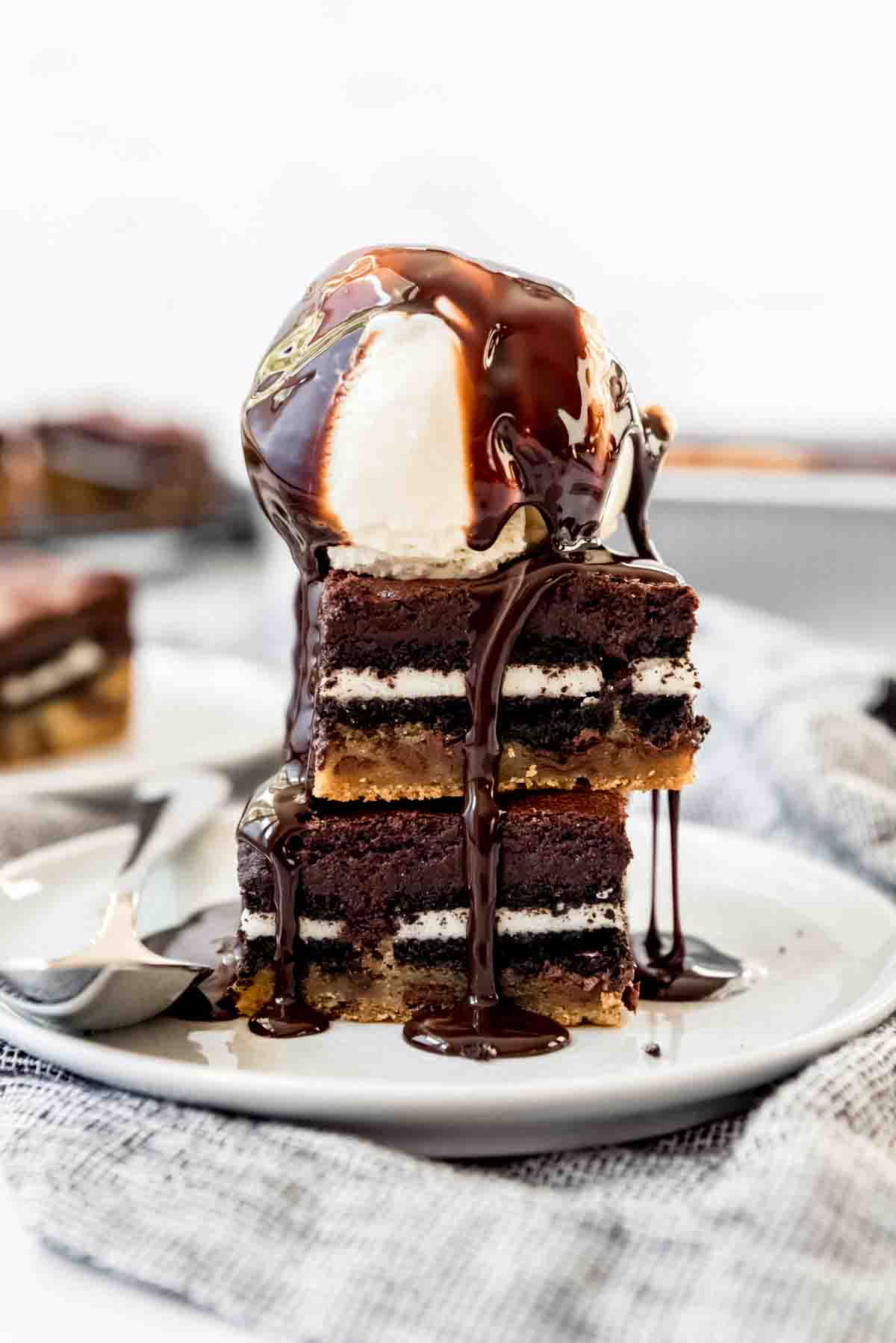 Two slutty brownies stacked on a plate with a scoop of vanilla ice cream on top.