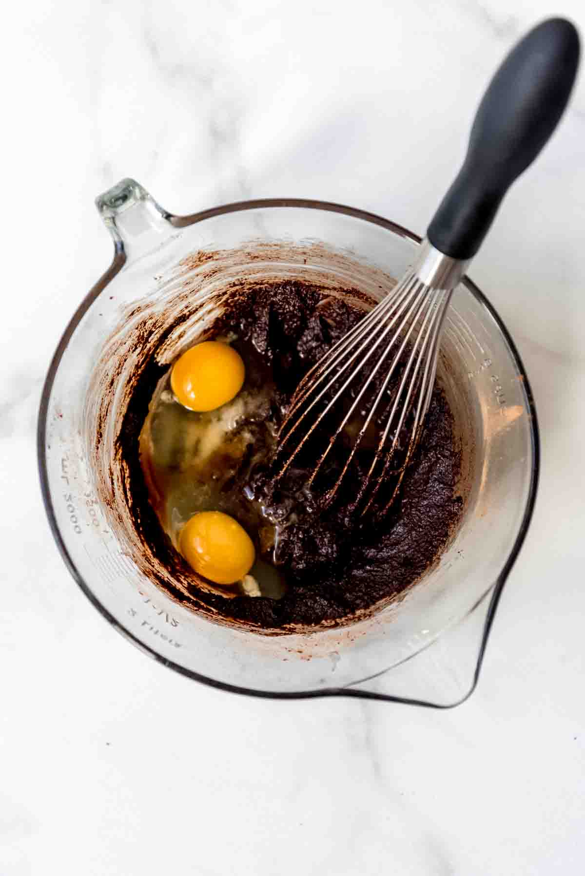 adding eggs to the brownie batter with a whisk