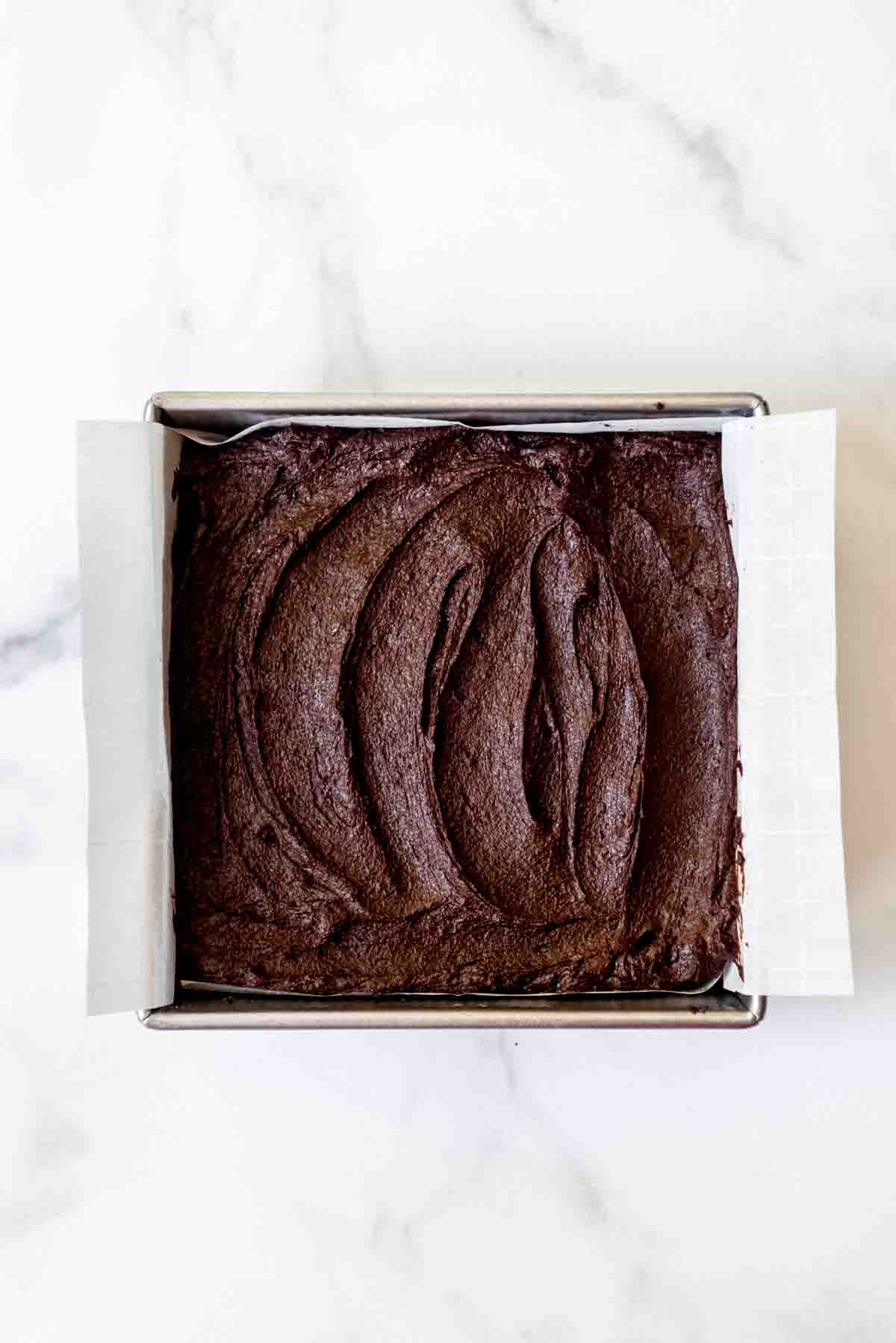 brownie batter spread on top of the slutty brownie layers in an 8x8 baking pan