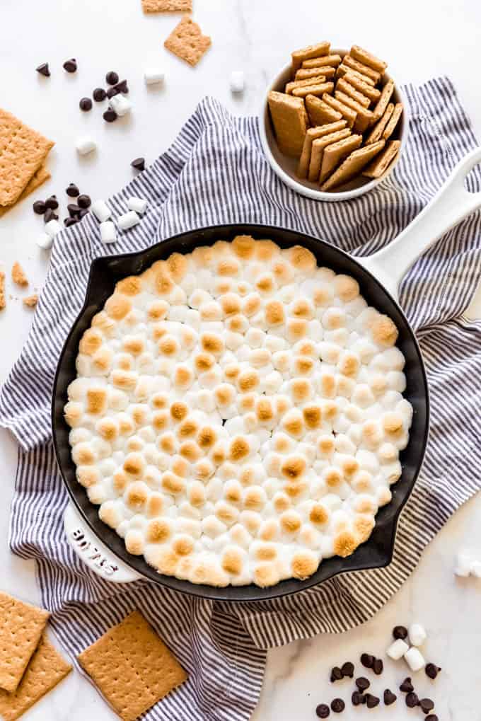 a skillet filled with chocolate and toasted marshmallows next to graham cracker sticks