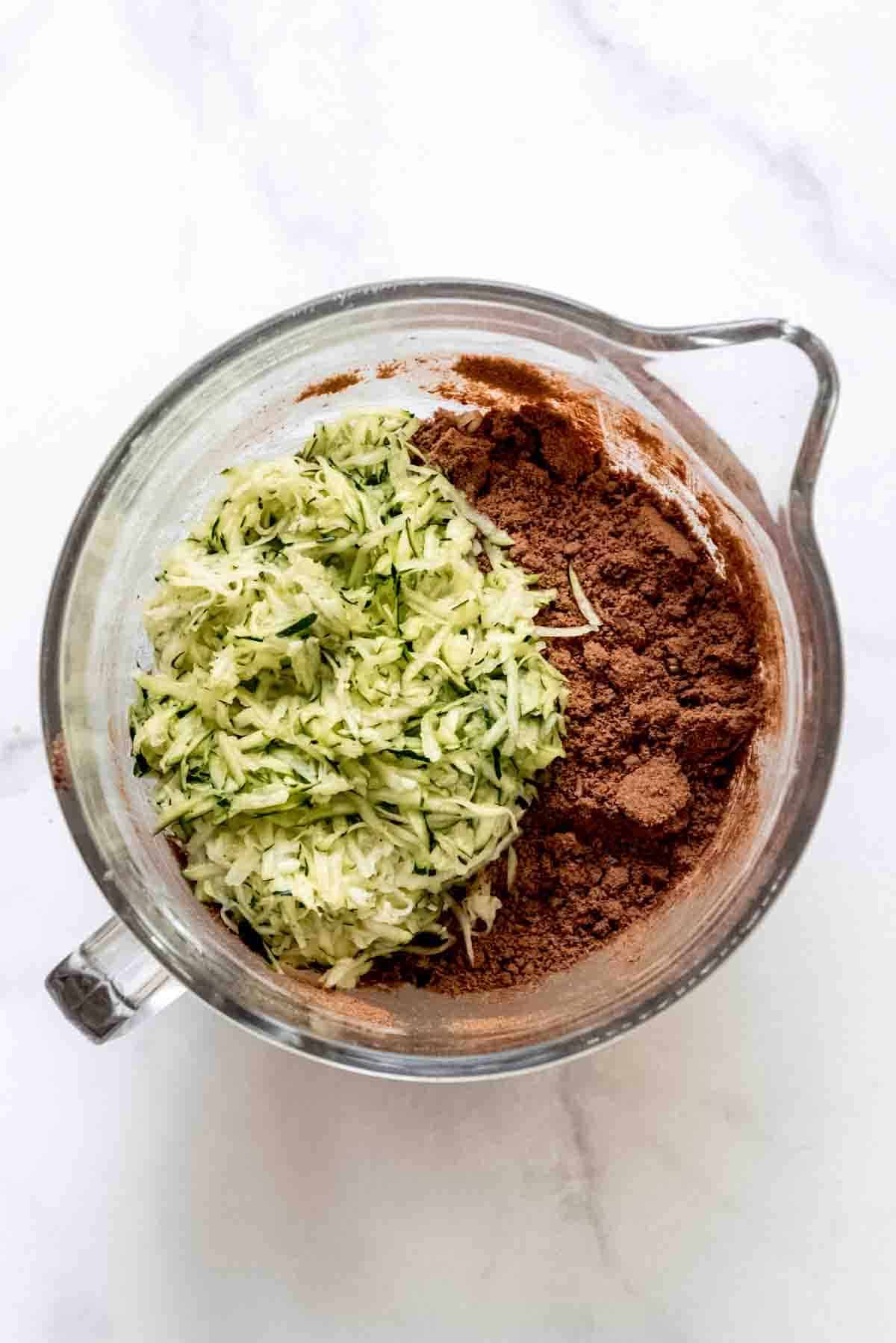 Shredded zucchini added to a bowl of dry brownie mix.