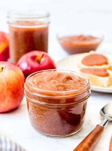 A half-pint jar of apple butter next to a spoon and apples.