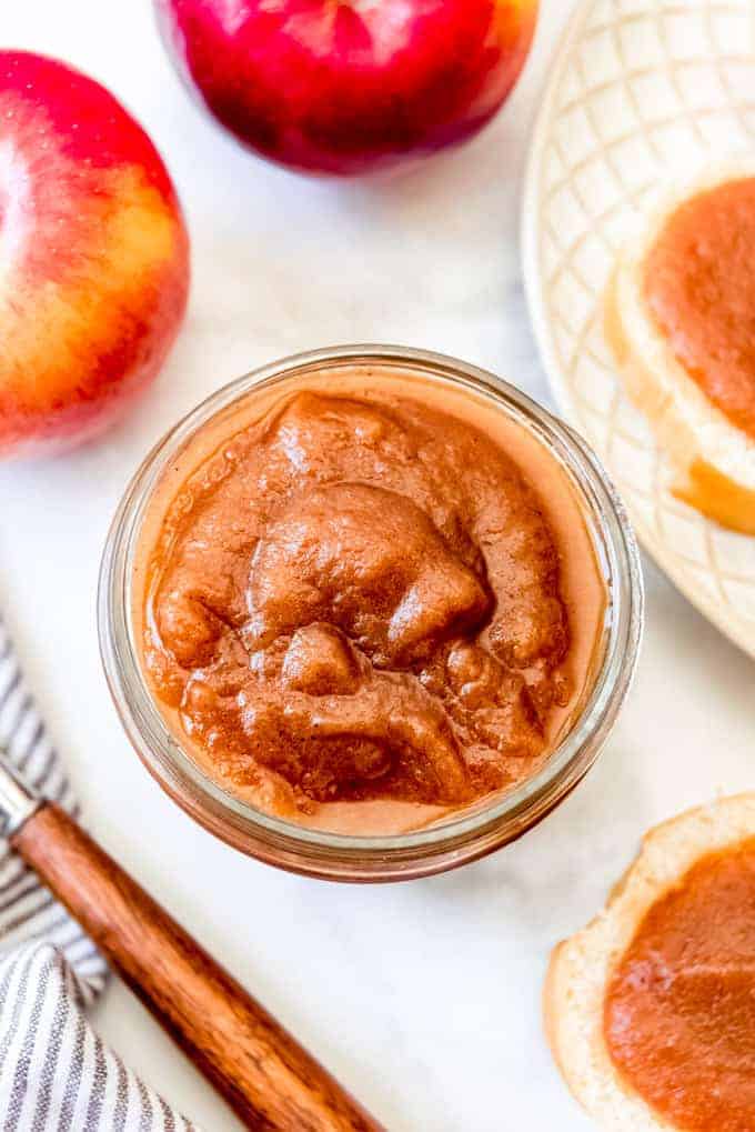 Smooth homemade apple butter in a jar next to red apples.