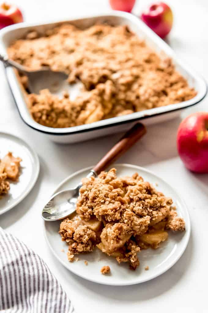 A scoop of homemade apple crisp on a dessert plate in front of the rest of the apple crisp in the pan.