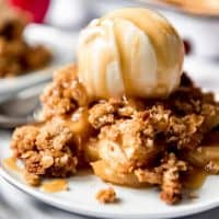 A scoop of caramel drizzled ice cream over a plate full of apple crisp