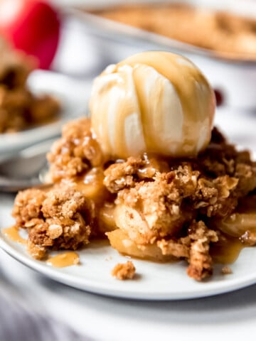 A scoop of caramel drizzled ice cream over a plate full of apple crisp