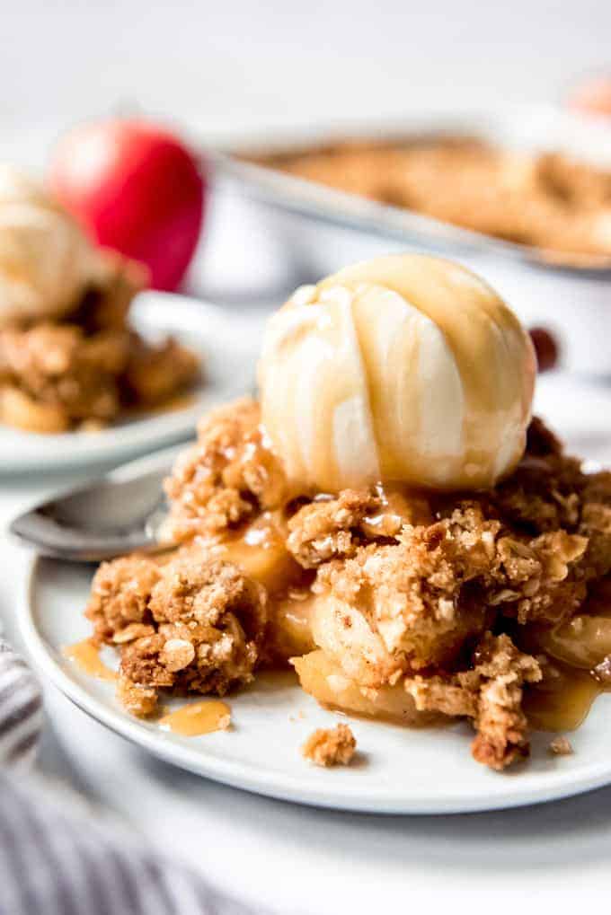 Apple crisp on a plate with a scoop of ice cream and caramel syrup drizzled on top.