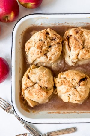Four apple dumplings cooked in a baking pan with cinnamon syrup.