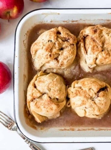 Four apple dumplings cooked in a baking pan with cinnamon syrup.