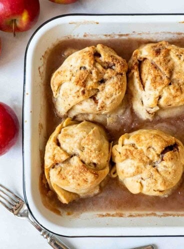 Four apple dumplings cooked in a baking pan with cinnamon syrup.