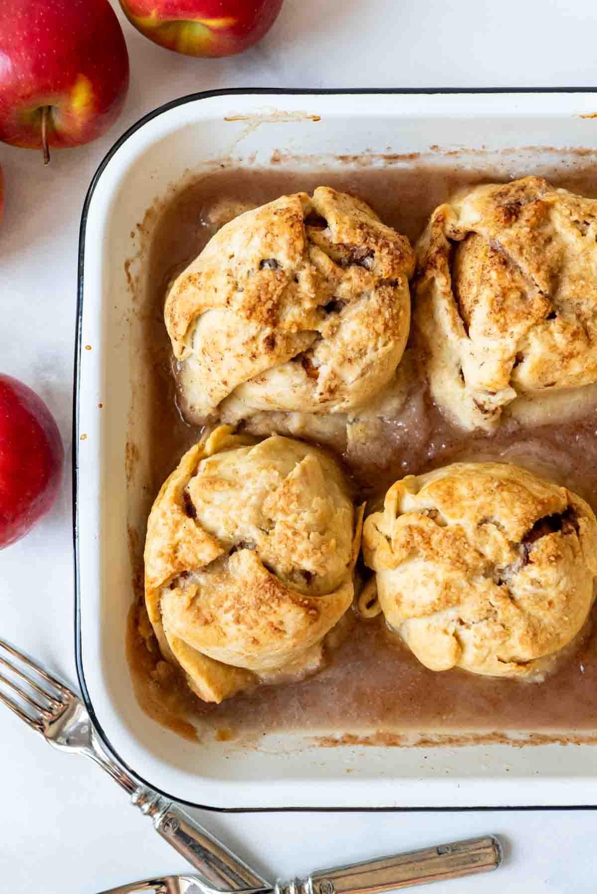 Four apple dumplings cooked in a baking pan with cinnamon syrup.