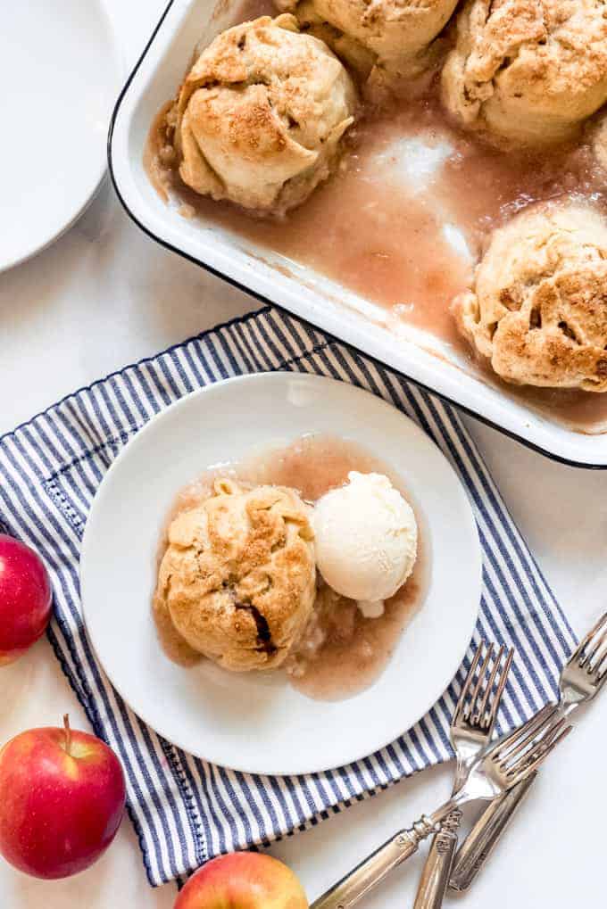 An apple dumpling on a plate with ice cream next to a pan with more apple dumplings.