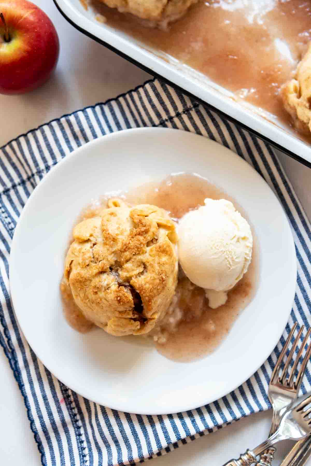 An apple dumpling on a white plate with a scoop of vanilla ice cream.