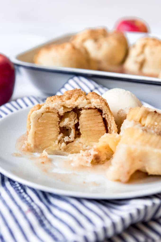 An apple dumpling that has been sliced in half to show the inside on a plate.