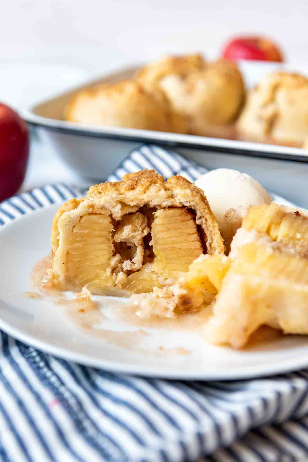 An apple dumpling that has been sliced in half to show the inside on a plate.