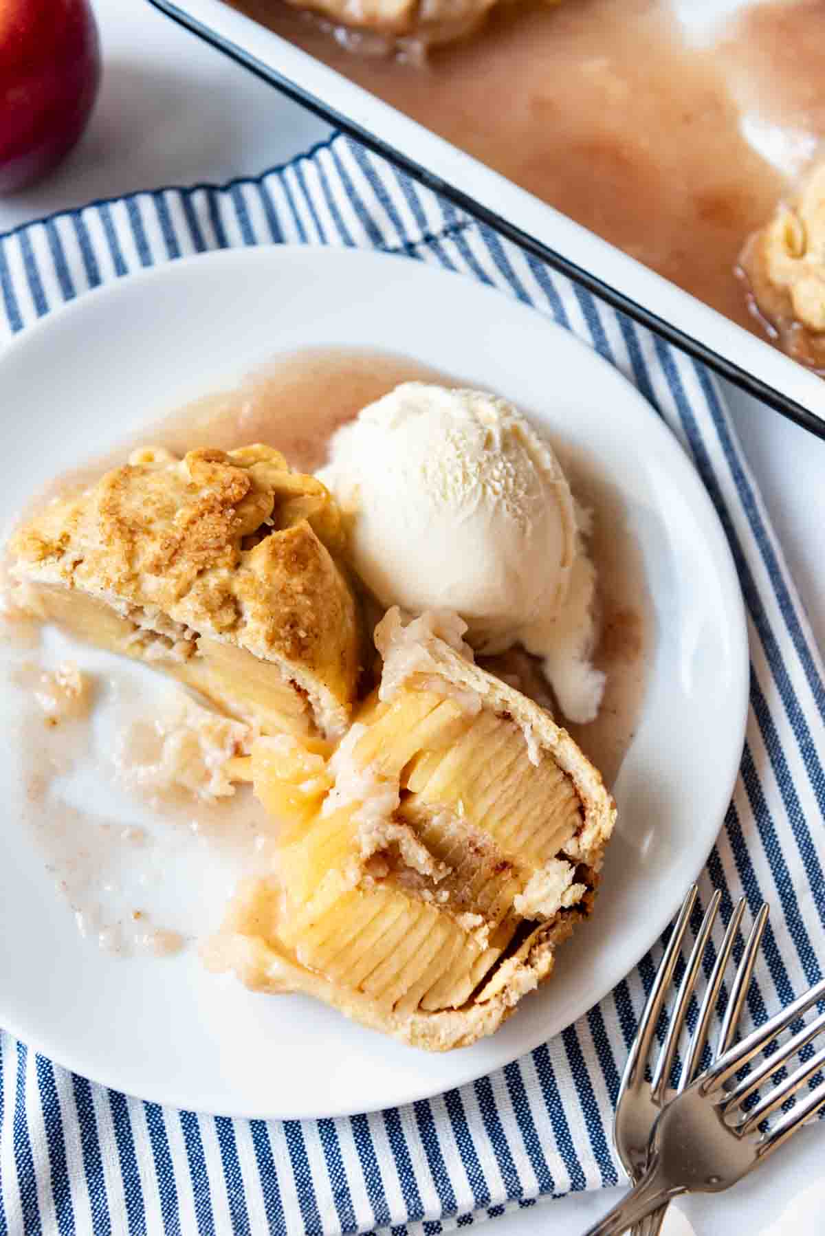 An apple dumpling sliced open on a white dessert plate with a scoop of ice cream.