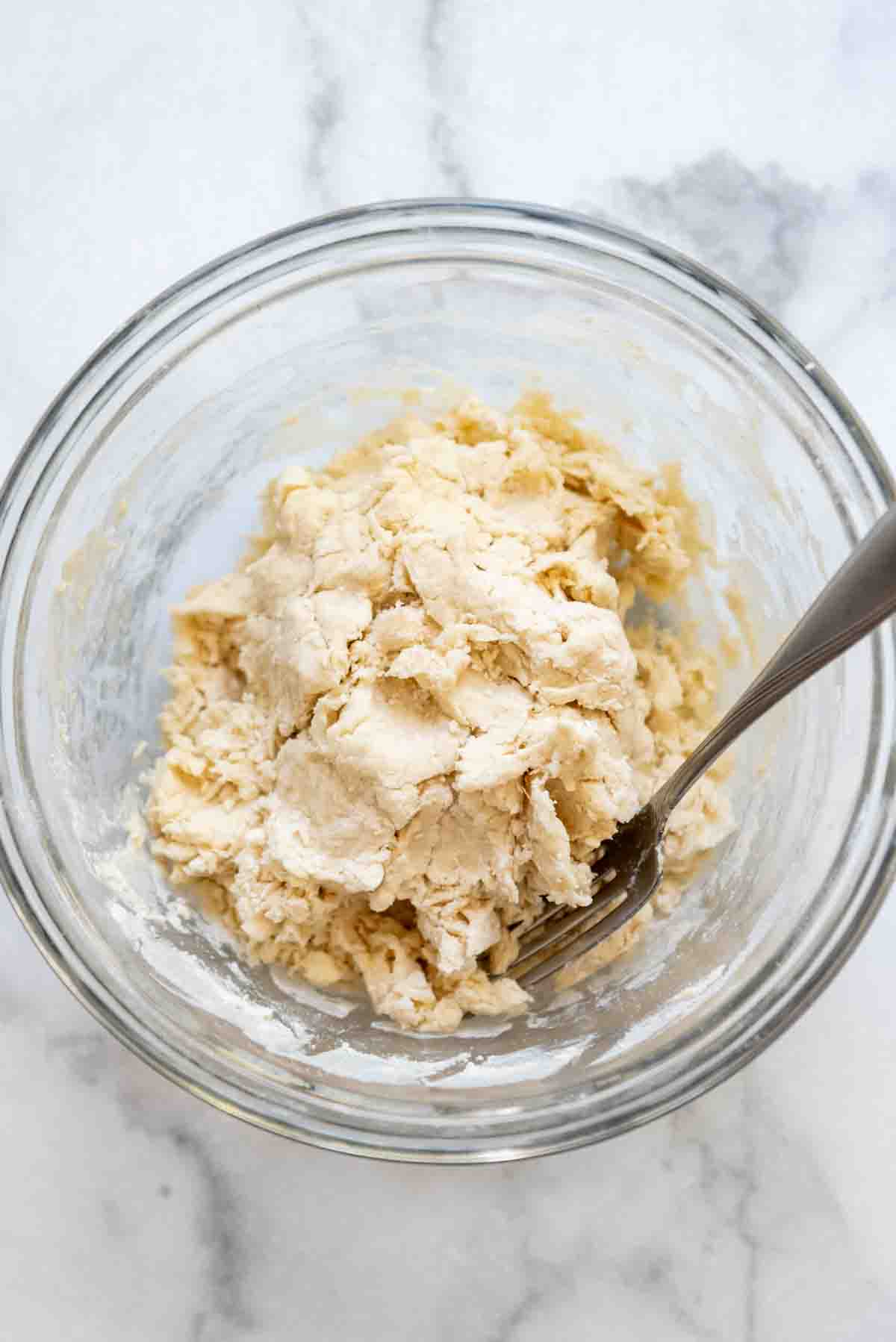 a bowl of dough for dumplings coming together in a glass bowl with a fork