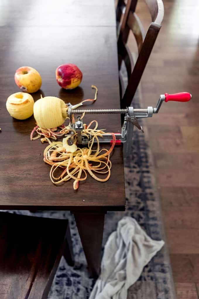 An apple peeler and corer fixed to a wooden table being used to peel an apple.