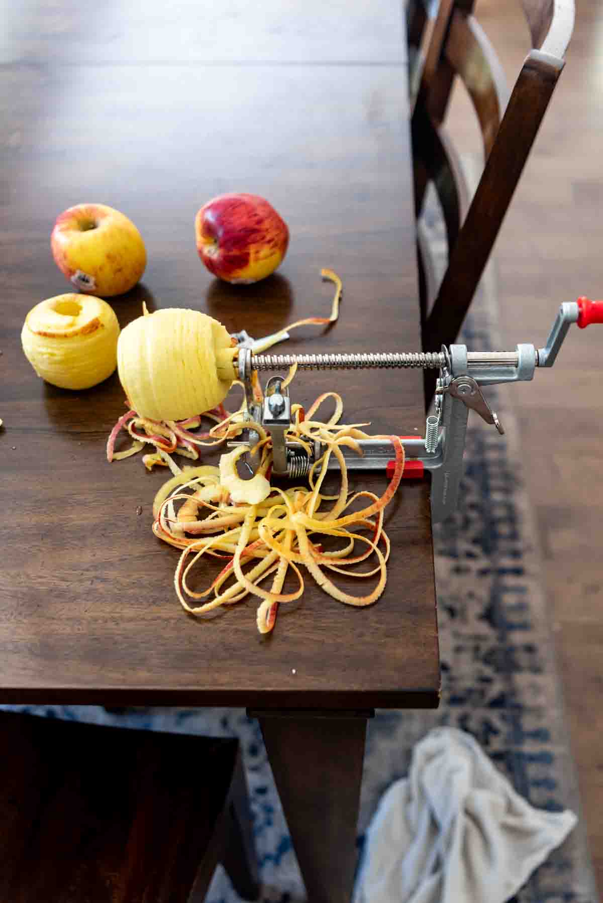 An apple peeler and corer fixed to a wooden table being used to peel an apple.