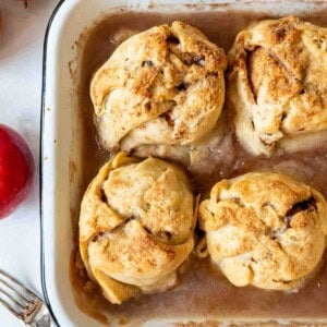 Four apple dumplings cooked in a baking pan with cinnamon syrup.