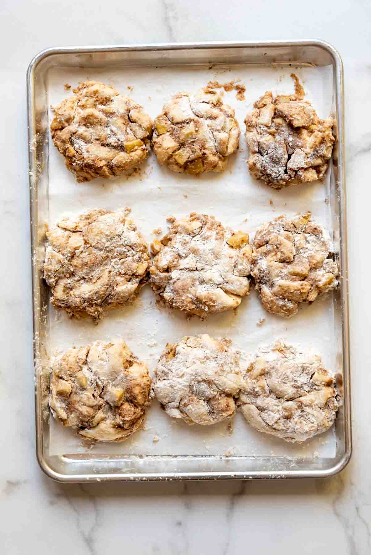 Apple fritter dough resting on a baking sheet lined with parchment paper.