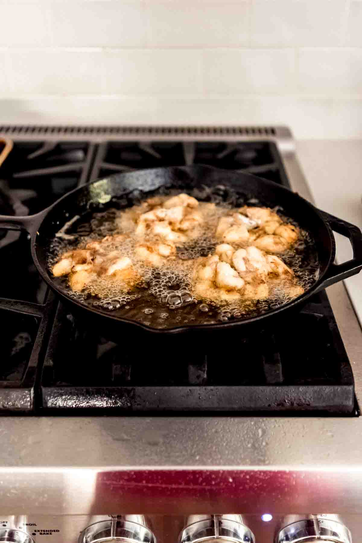 Apple fritters frying in oil in a large skillet on the stove.