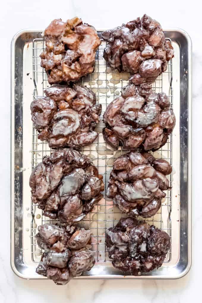 Glazed apple fritters on a wire rack set over a baking sheet.