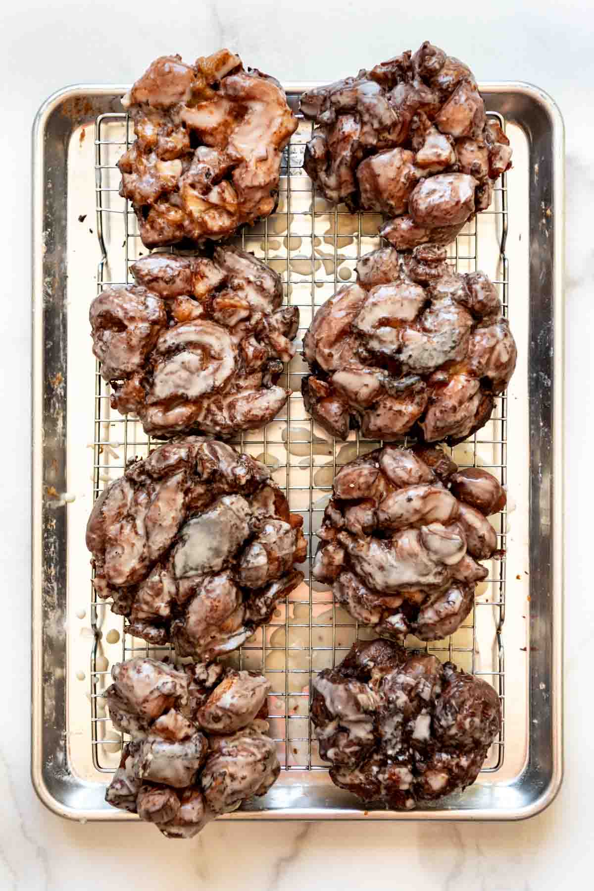 Glazed apple fritters on a wire rack set over a baking sheet.