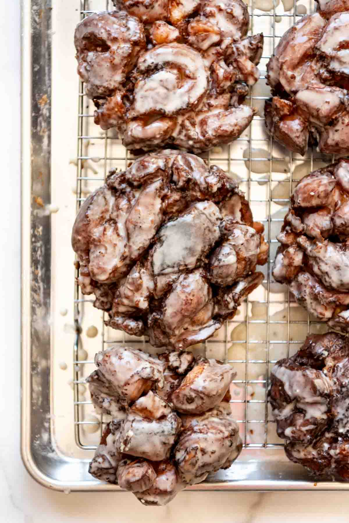 Glazed apple fritters on a wire rack.