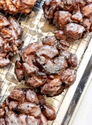 Glazed apple fritters on a wire rack.