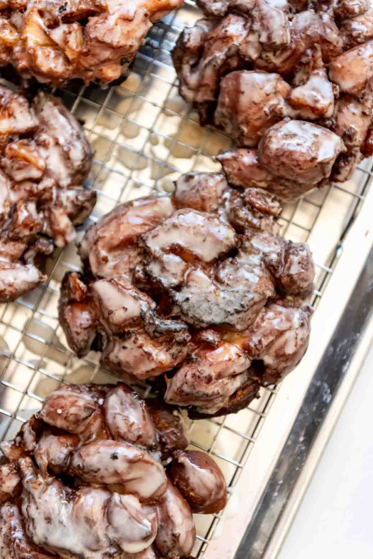 Glazed apple fritters on a wire rack.