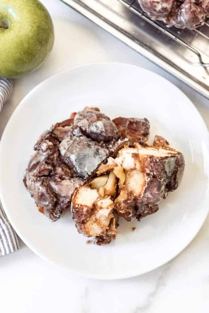 A torn apart apple fritter on a white plate.