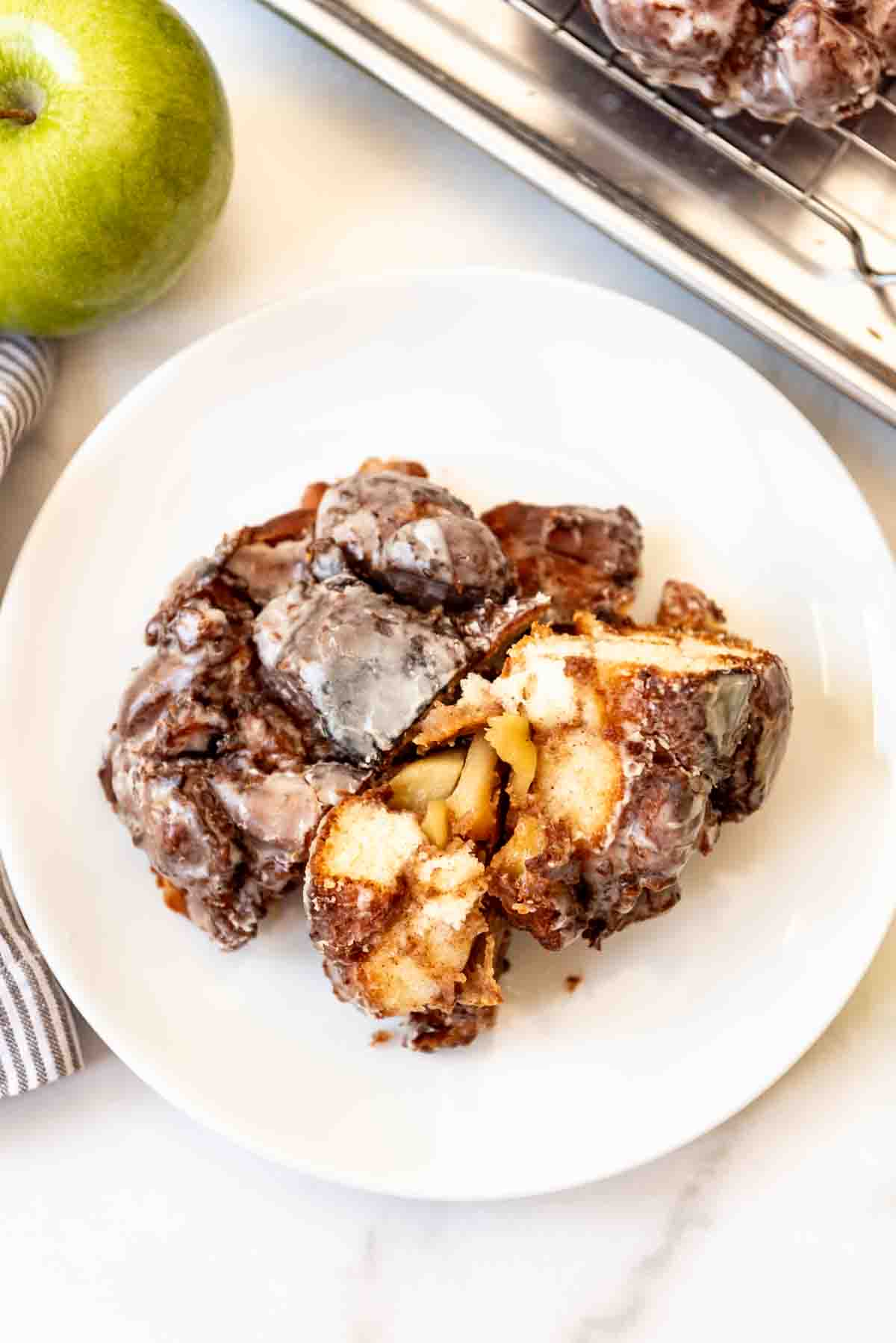 A torn apart apple fritter on a white plate.