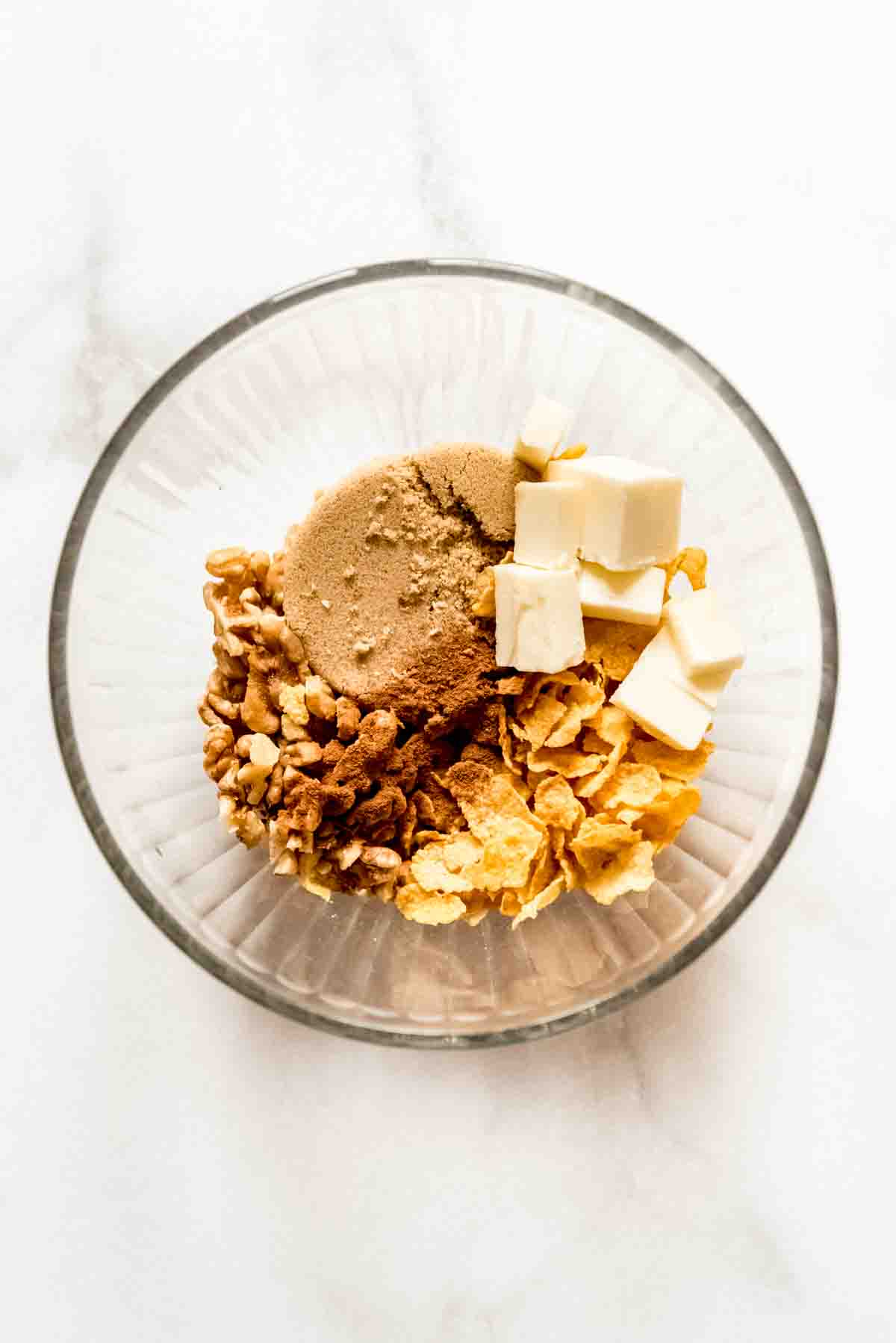 A glass bowl filled with cinnamon, walnuts, brown sugar, butter, and cornflakes.