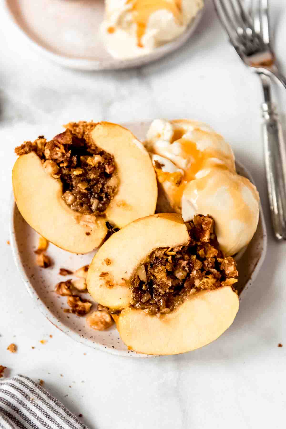 A baked apple filled with cinnamon brown sugar filling that is sliced in half and served on a plate with ice cream and caramel sauce.