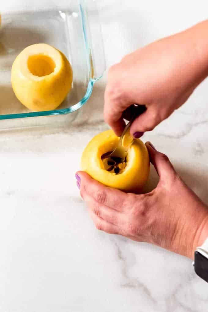 Hands holding a yellow apple and scooping out the core with a metal teaspoon.