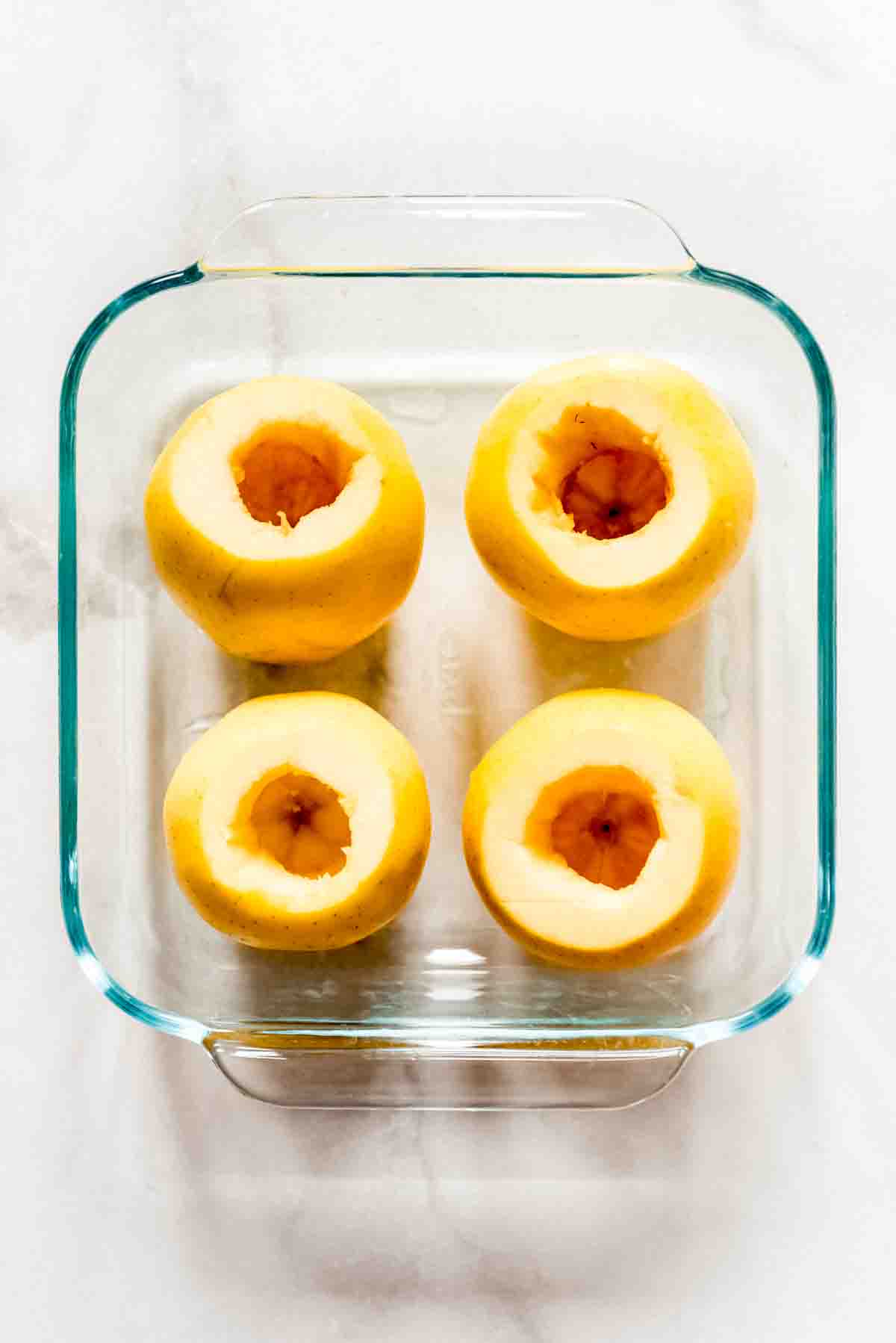 4 hollowed out apples in a square glass baking dish