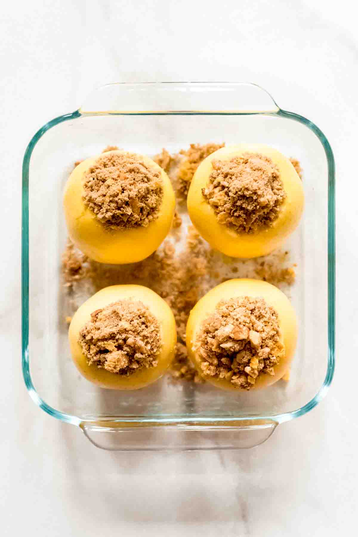 4 apples filled with ingredients and placed in a glass baking dish for baked apples